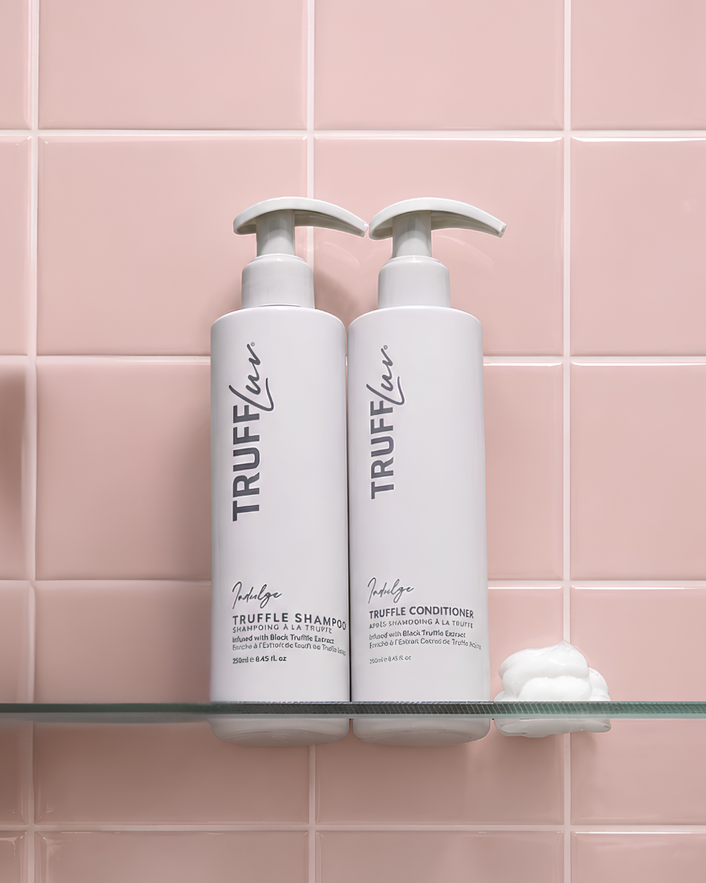 Two white Truffluv Truffle Shampoo and Truffle Conditioner pump bottles displayed side-by-side on a glass shelf against a pink tiled wall.